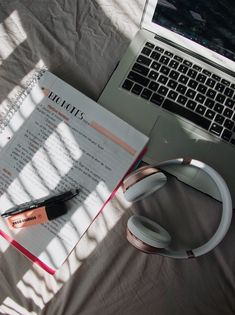 an open notebook and headphones on top of a bed next to a laptop computer