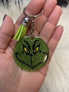 a hand holding a green glitter keychain with an angry grin face on it