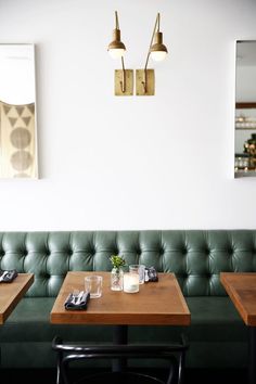 two tables with place settings on them in front of a green couch and mirror behind them