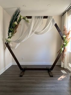 a wedding arch decorated with flowers and greenery in the middle of an empty room