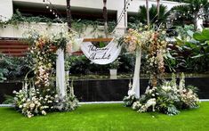 an outdoor ceremony setup with flowers and greenery on the grass in front of a building