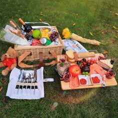 a picnic basket filled with food on top of a grass covered field next to utensils