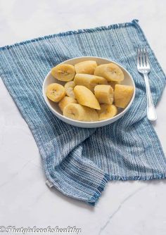 a white bowl filled with cut up bananas on top of a blue towel next to a fork