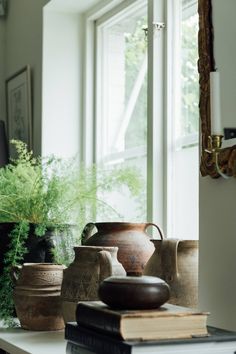 vases and books are sitting on a table in front of a window with a potted plant