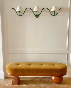 a bench with three lamps mounted on the wall behind it in a room that has wood floors and white walls