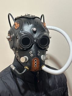 a man wearing a gas mask with goggles and pipes attached to his face is standing in front of a white wall