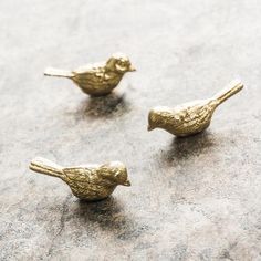 three small gold birds sitting on top of a cement floor next to eachother