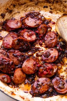 cooked sausages and onions in a skillet with a wooden spoon