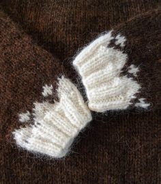 a knitted mitten laying on top of a brown and white sweater with holes in it