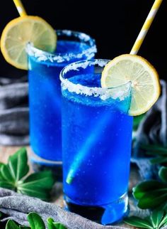 two blue cocktails with lemon wedges and garnishes on the rim