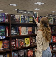 a woman standing in front of a bookshelf holding up a book to read