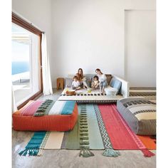 three people sitting on a couch in a living room with colorful rugs and pillows