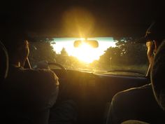 the sun is setting behind two people driving in a car with their heads turned to the side