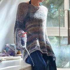 a woman sitting on a window sill wearing a knitted sweater and blue pants