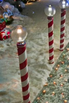 three red and white candy canes are in the snow near christmas lights on poles