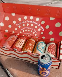 an open can of soda sitting next to some colorful tins on a counter top