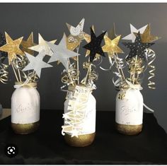 three mason jars filled with gold and silver stars on top of a black cloth covered table