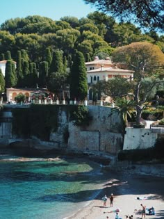 people are on the beach in front of an old wall and some buildings with trees