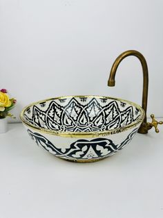 a decorative bowl with handles is sitting on a table next to a flower vase and a brass faucet