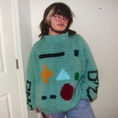 a woman standing in front of a door wearing a green sweater with colorful shapes on it