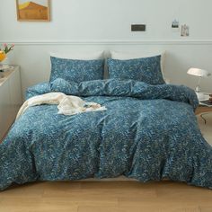 a bed with blue bedspread and pillows in a white room next to a window