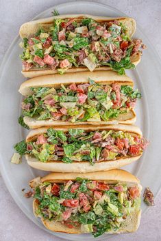 three hot dogs with lettuce, tomatoes and other toppings on a plate