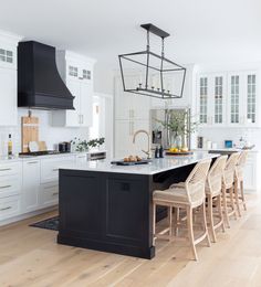 a kitchen with white cabinets, black island and wooden chairs in front of the counter