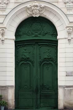 a large green door on the side of a building with two potted plants in front of it