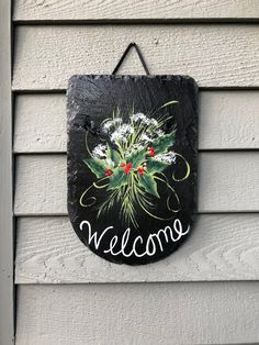 a welcome sign is hanging on the side of a house with holly and berries painted on it