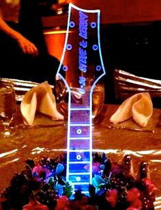 a guitar shaped cake sitting on top of a table covered in frosting and flowers