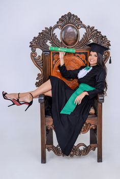 a woman sitting on top of a wooden chair wearing a graduation gown and holding a book