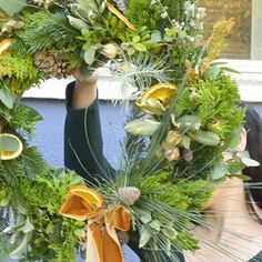 a woman is holding up a wreath with oranges and greenery on the front