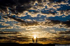 two people standing on top of a grass covered hill under a cloudy blue and yellow sky