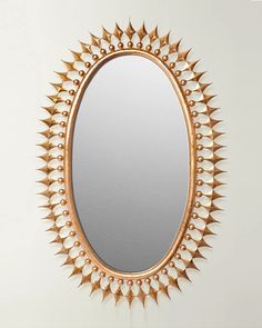 an oval mirror with gold spikes on the edges and a white wall in the background