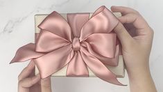 a person holding a pink bow on top of a white box