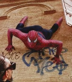 a man in a spiderman suit laying on the ground next to a graffiti covered wall