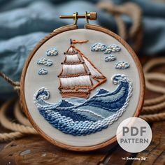 an embroidered sailboat with waves and clouds is shown on a wooden table next to rope