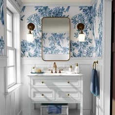 a bathroom with blue and white wallpaper, gold fixtures and a large mirror above the sink