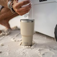 a person is pouring something into a cup in the sand near a cooler and tire