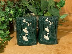 two green vases sitting on top of a wooden table next to a potted plant