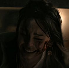 a woman is laughing and holding her head in the dark with blood all over her face