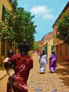 two women walking down a street with trees in the back ground and people on either side