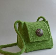 a small green purse with a button on the front and shoulder strap, sitting on a white surface