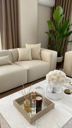 a living room filled with furniture and flowers on top of a white coffee table in front of a window