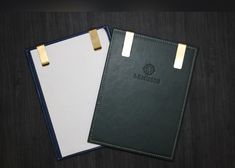 two notebooks sitting next to each other on top of a wooden table with gold trimming