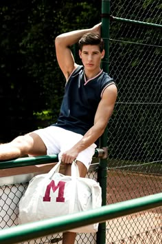 a young man sitting on a fence holding a white duffel bag with the letter m in it