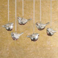 four silver birds hanging from strings on a brown wall with red berries in the beaks