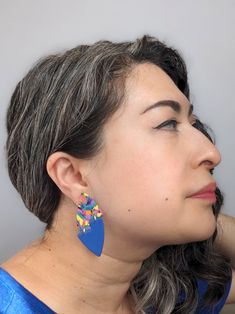 a woman with grey hair wearing blue earrings and looking off into the distance while standing in front of a gray wall