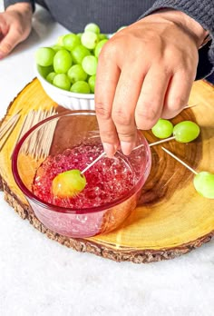 a person is dipping something into a bowl with green grapes in the background on a wooden plate