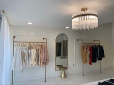 a closet with clothes hanging on the wall and a chandelier above it, in front of a mirror